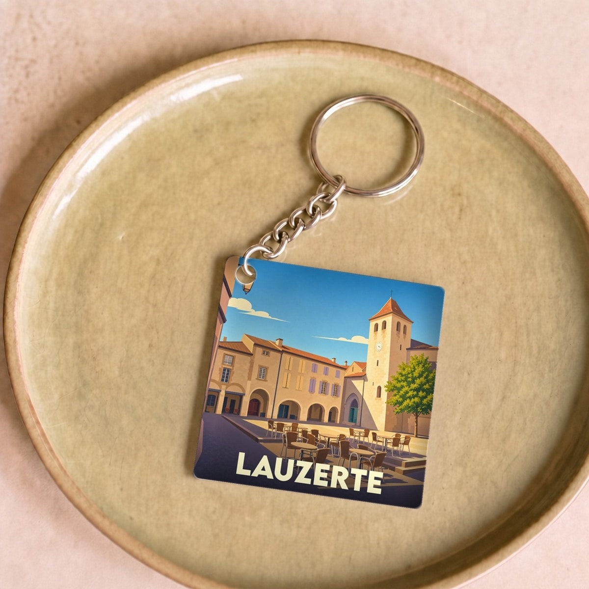 Porte-clés souvenir de la ville de Lauzerte avec une illustration stylisée de sa place centrale.