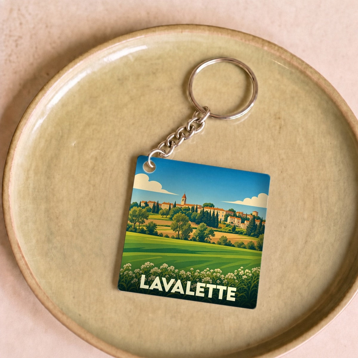 Porte-clés souvenir de la ville de Lavalette avec une illustration stylisée de son paysage champêtre.