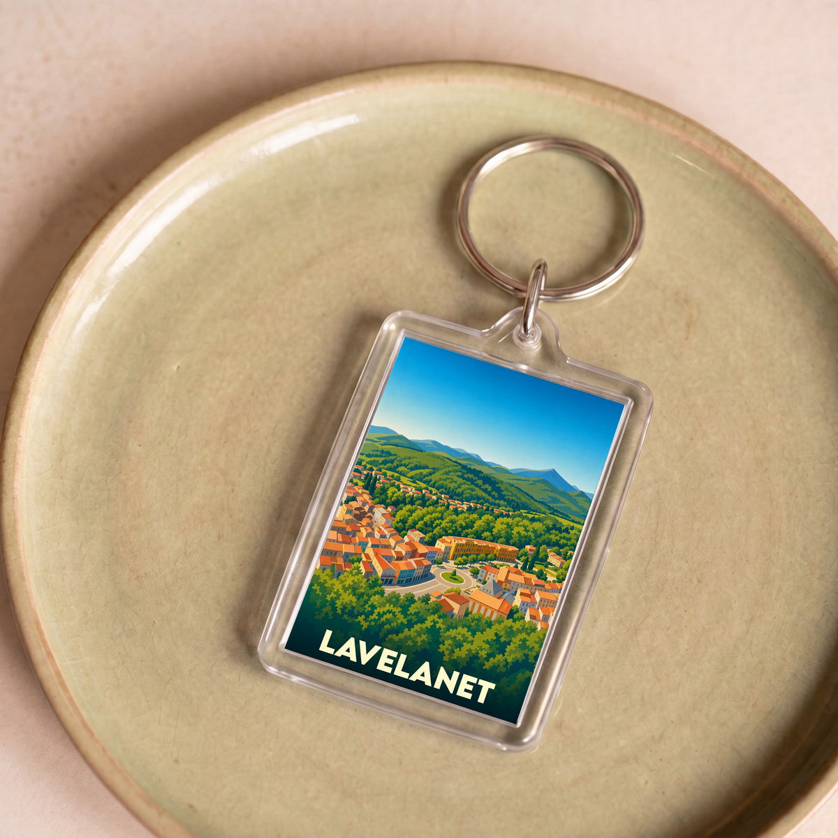 Porte-clés souvenir de la ville de Lavelanet avec une illustration stylisée d'un paysage urbain et montagneux.