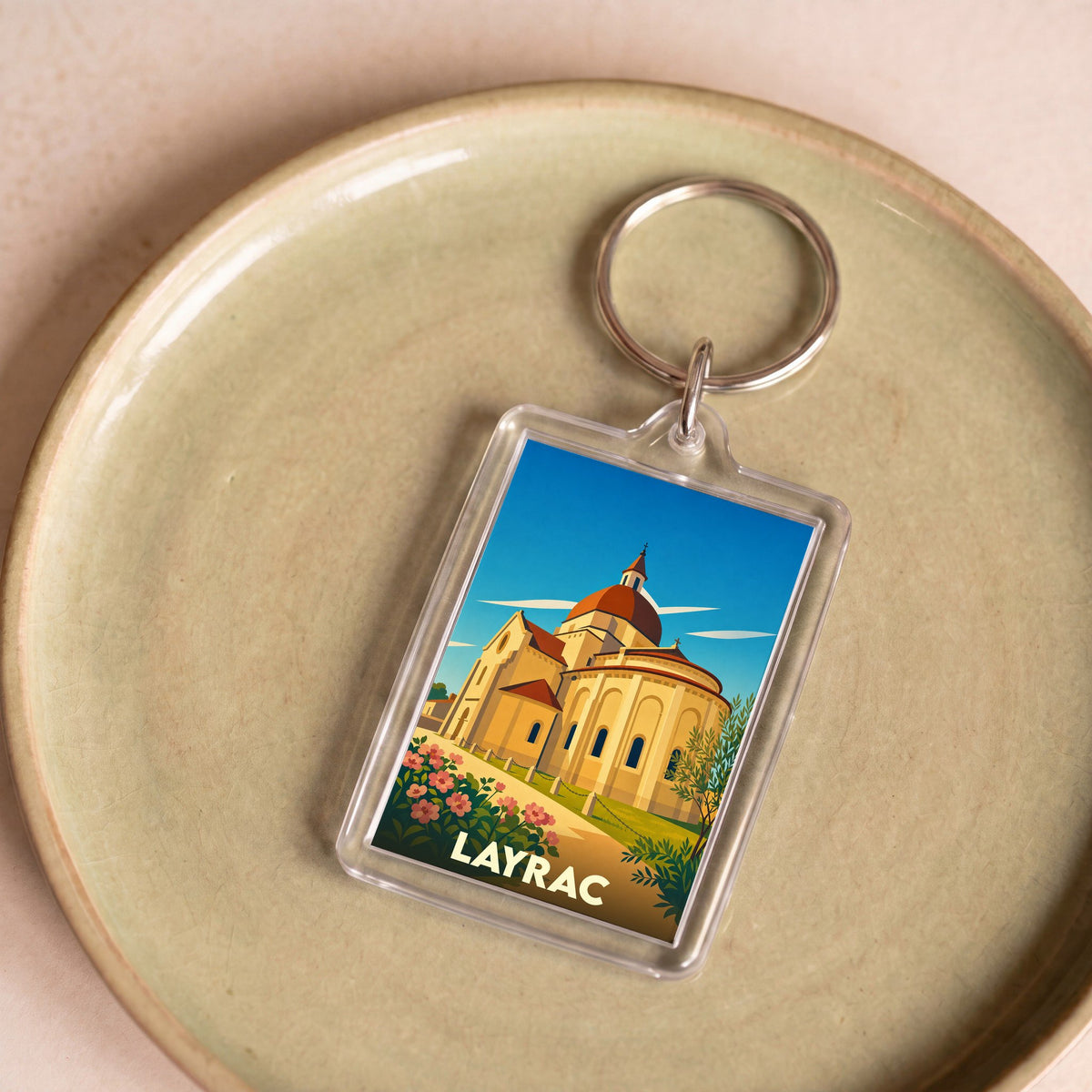 Porte-clés souvenir de la ville de Layrac avec une illustration stylisée de son église romane.