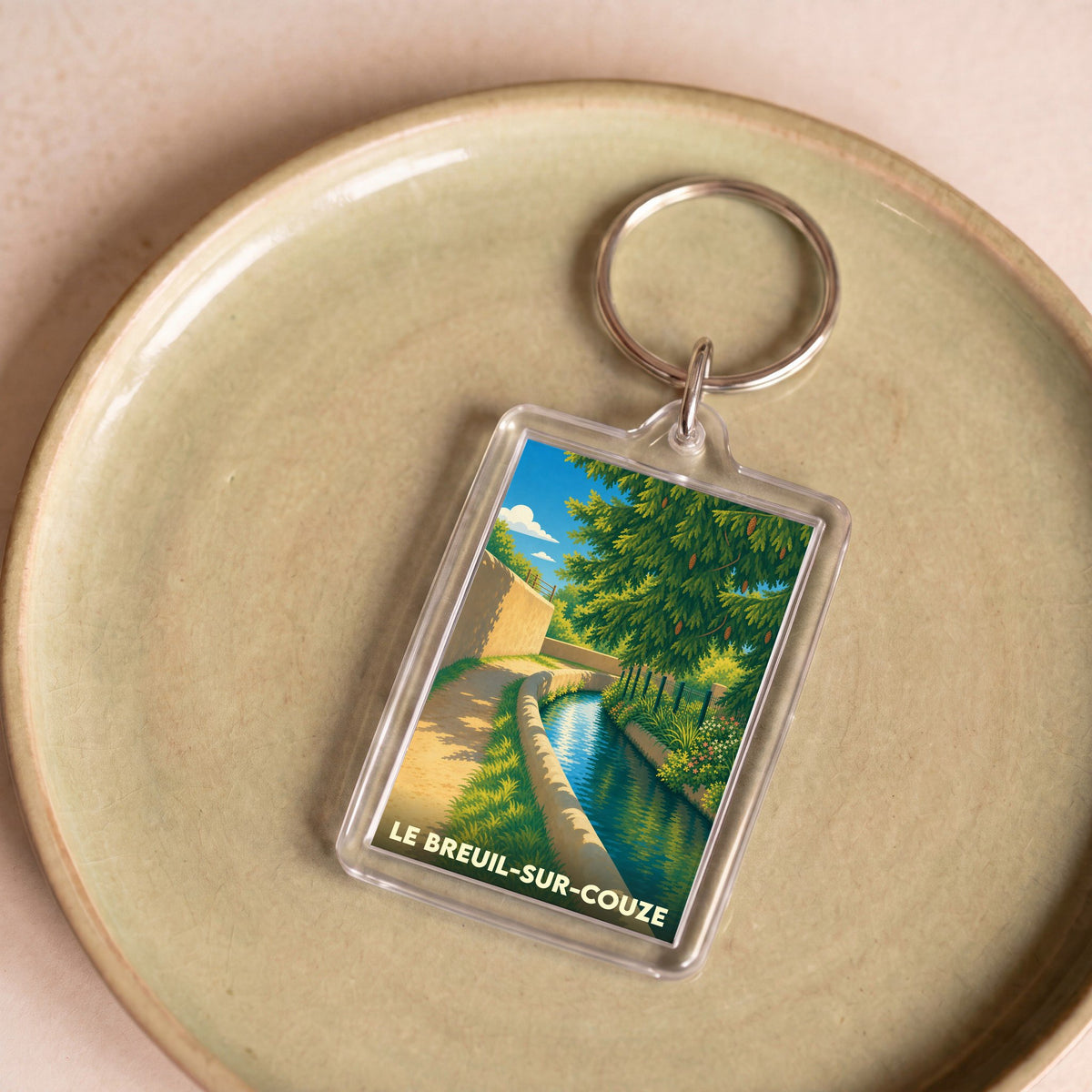 Porte-clés souvenir de la ville de Le Breuil-sur-Couze avec une illustration stylisée d'un canal arboré.