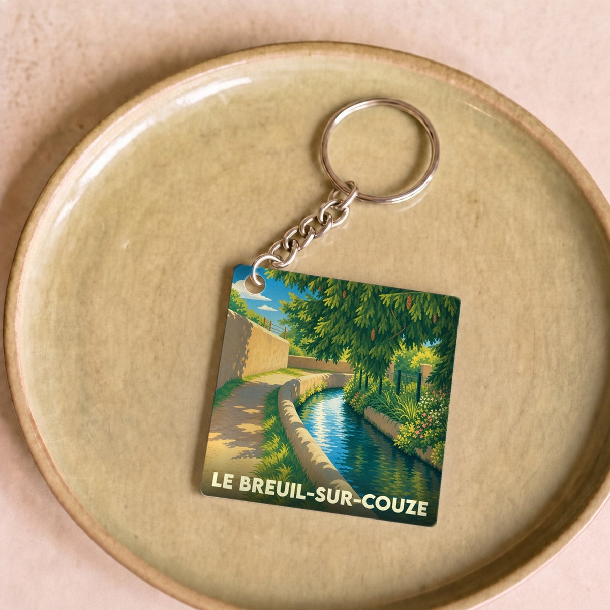 Porte-clés souvenir de la ville de Le Breuil-sur-Couze avec une illustration stylisée d'un canal arboré.
