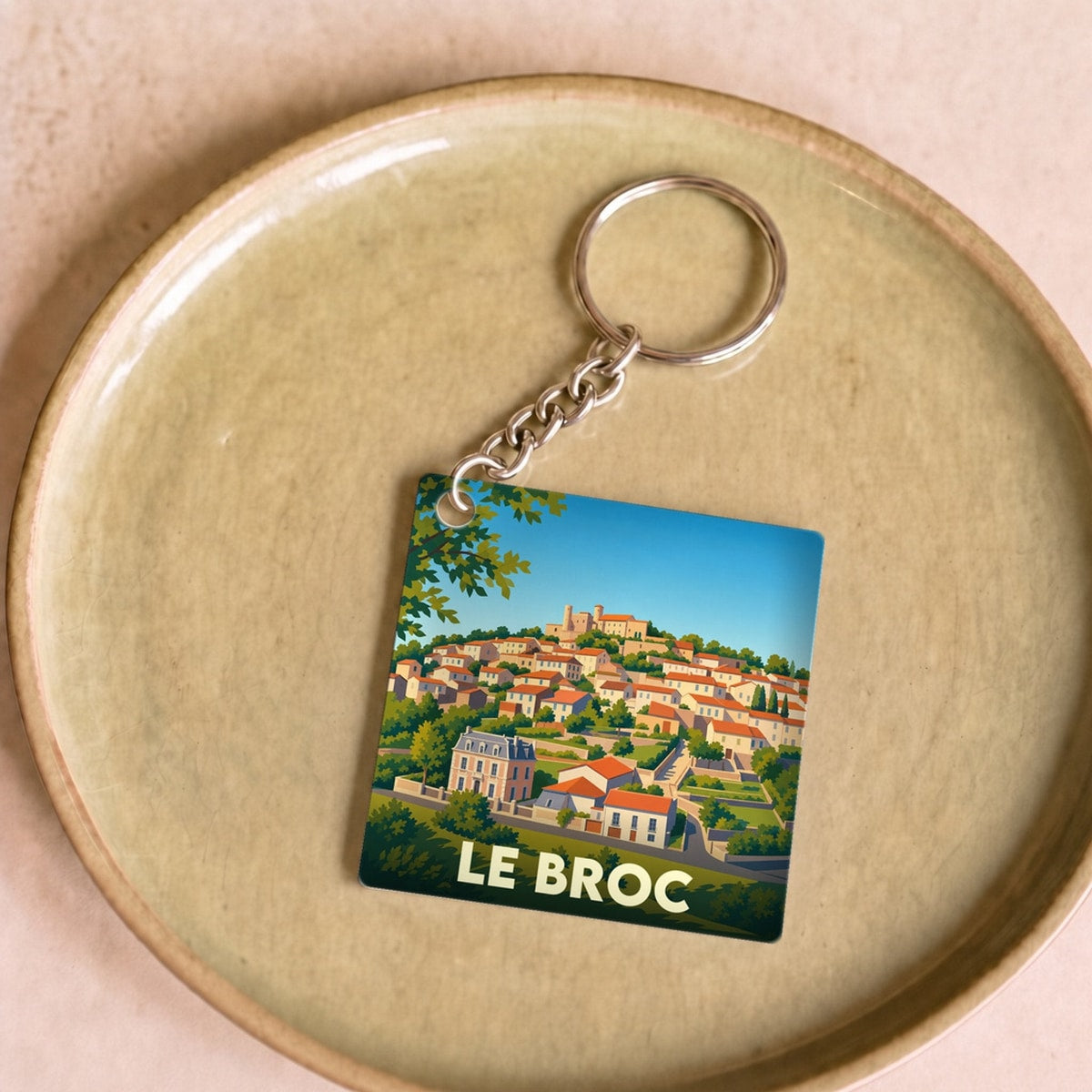 Porte-clés souvenir de la ville de Le Broc avec une illustration stylisée d'un village perché.