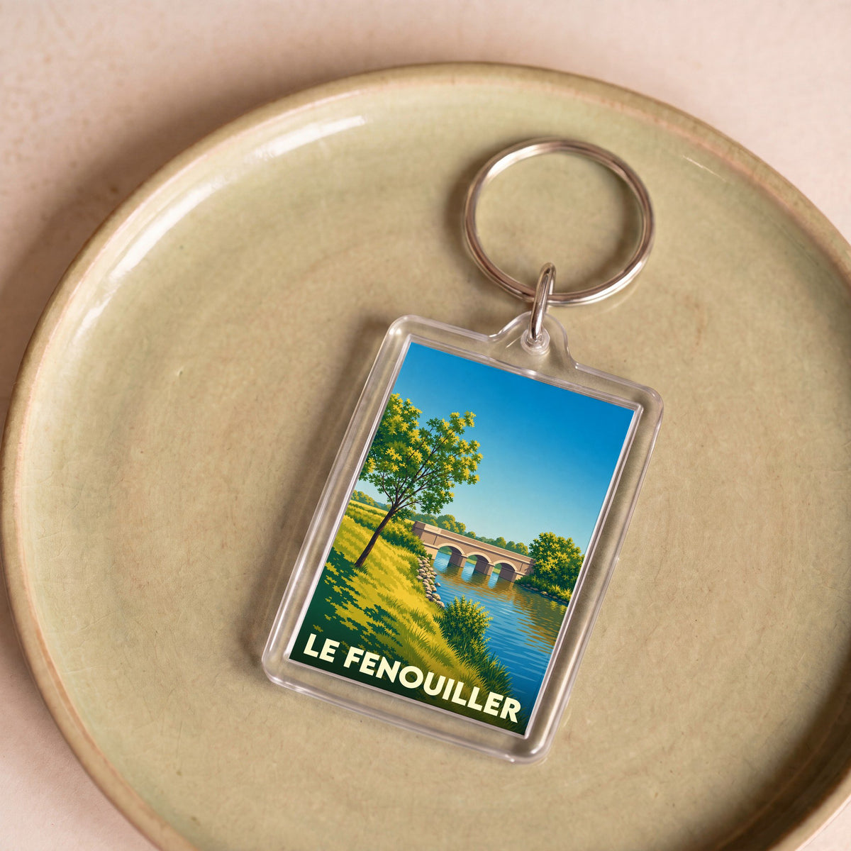 Porte-clés souvenir de la ville de Le Fenouiller avec une illustration stylisée d'un pont au bord de l'eau.