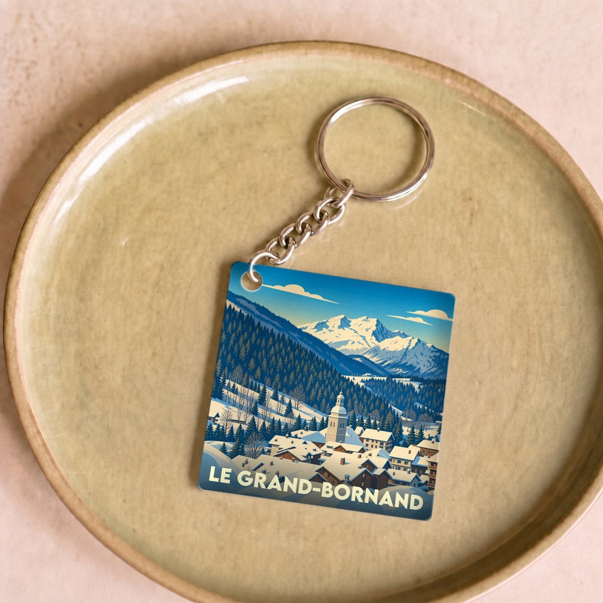 Porte-clés souvenir de la ville du Grand-Bornand avec une illustration stylisée d'un village de montagne enneigé.