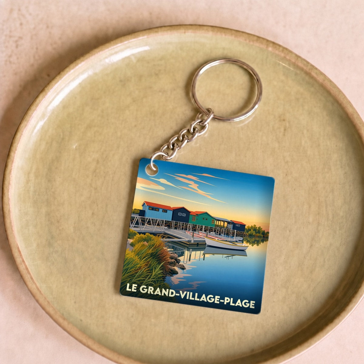 Porte-clés souvenir de la ville de Le Grand-Village-Plage avec une illustration stylisée de cabanes colorées sur l'eau.