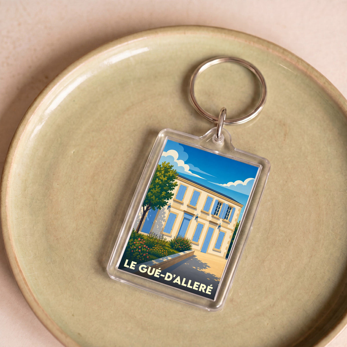 Porte-clés souvenir de la ville du Gué-d'Alleré avec une illustration stylisée d'une maison aux volets bleus.