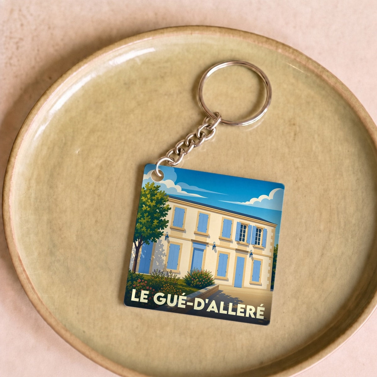 Porte-clés souvenir de la ville du Gué-d'Alleré avec une illustration stylisée d'une maison aux volets bleus.