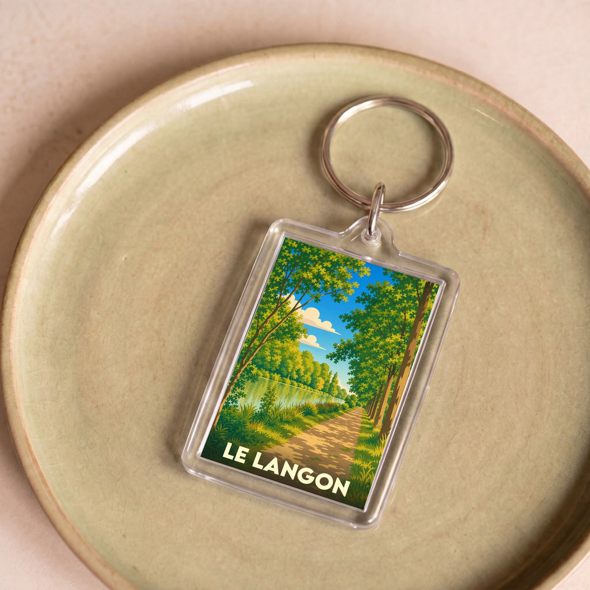 Porte-clés souvenir de la ville de Le Langon avec une illustration stylisée d'un chemin boisé en bord de rivière.