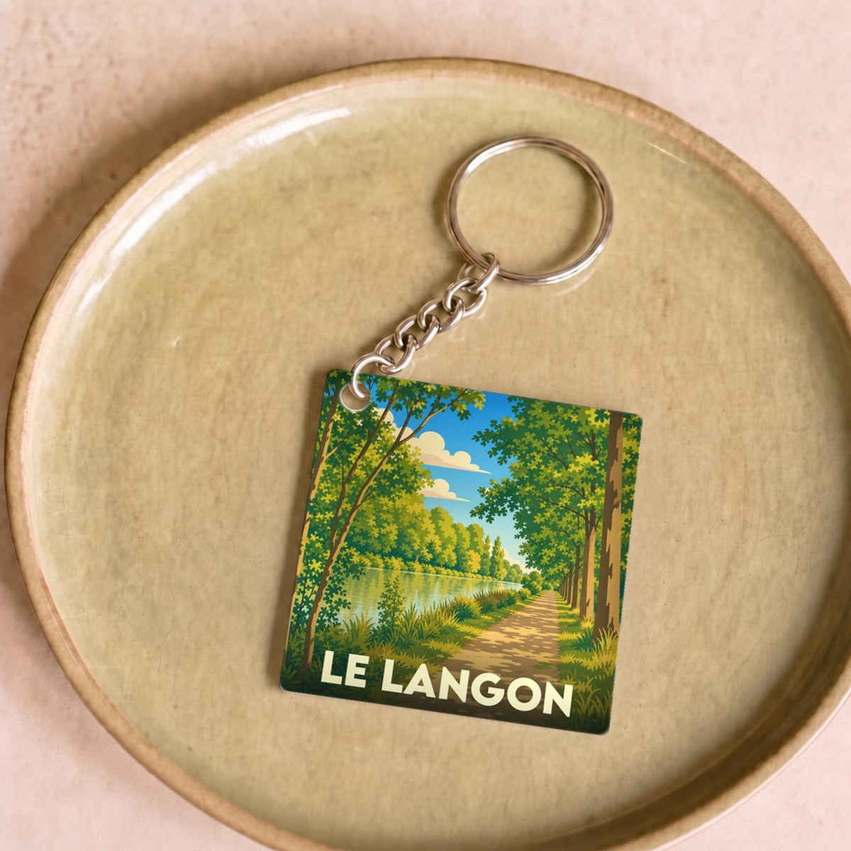 Porte-clés souvenir de la ville de Le Langon avec une illustration stylisée d'un chemin boisé en bord de rivière.