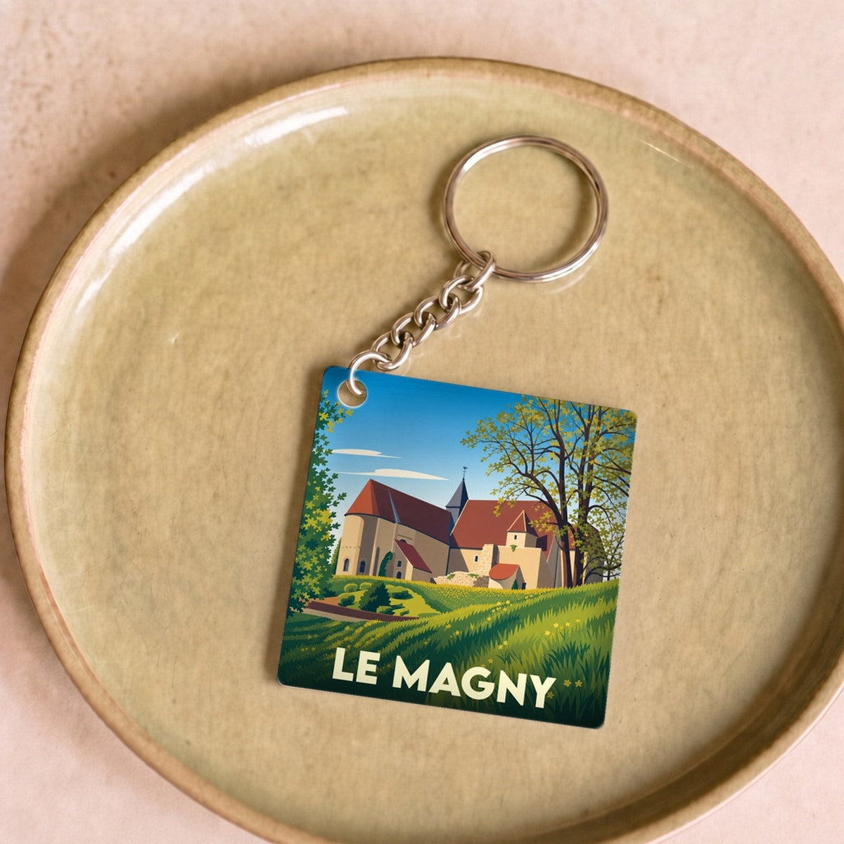Porte-clés souvenir de la ville de Le Magny avec une illustration stylisée d'un paysage champêtre.