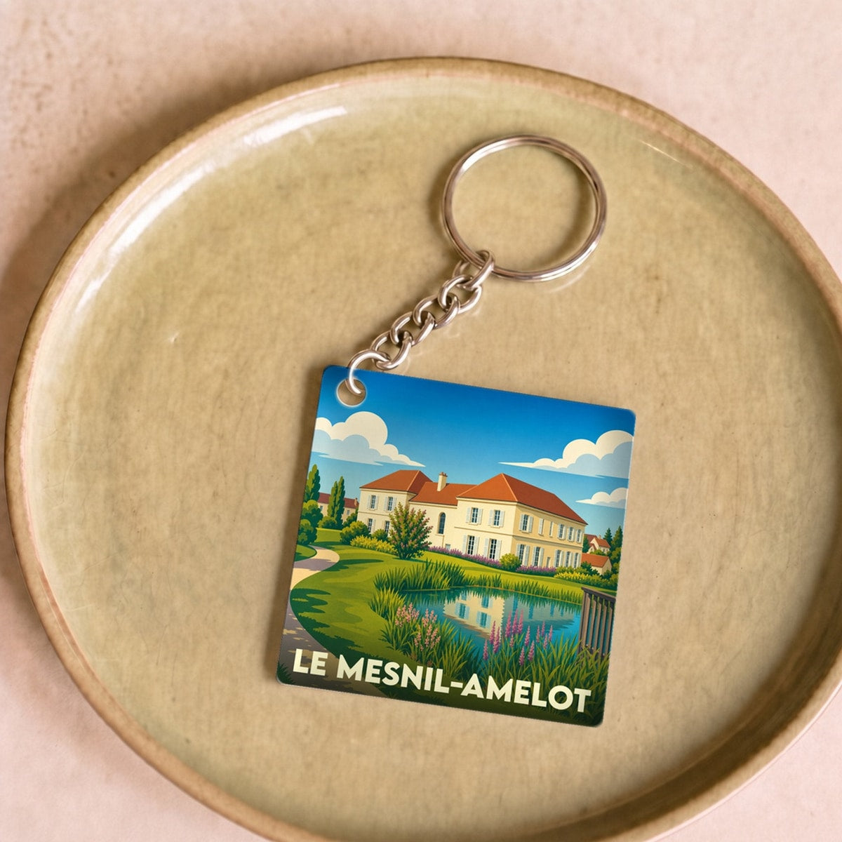 Porte-clés souvenir de la ville de Le Mesnil-Amelot avec une illustration stylisée d'un manoir et d'un étang.