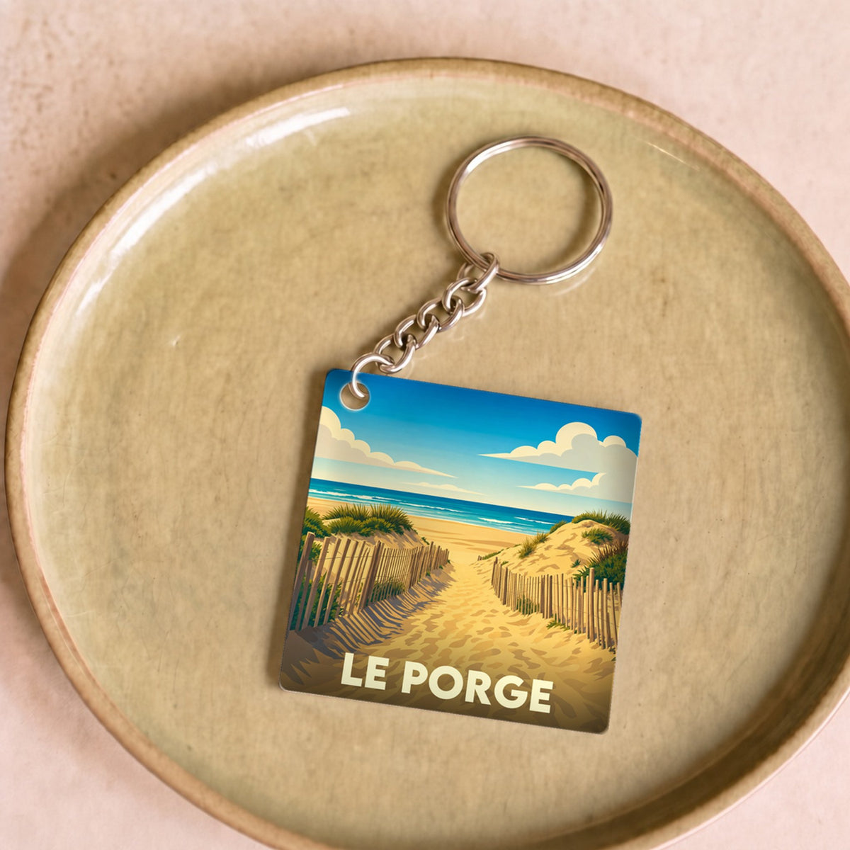Porte-clés souvenir de la ville du Porge avec une illustration stylisée d'un chemin dunaire menant à l'océan.