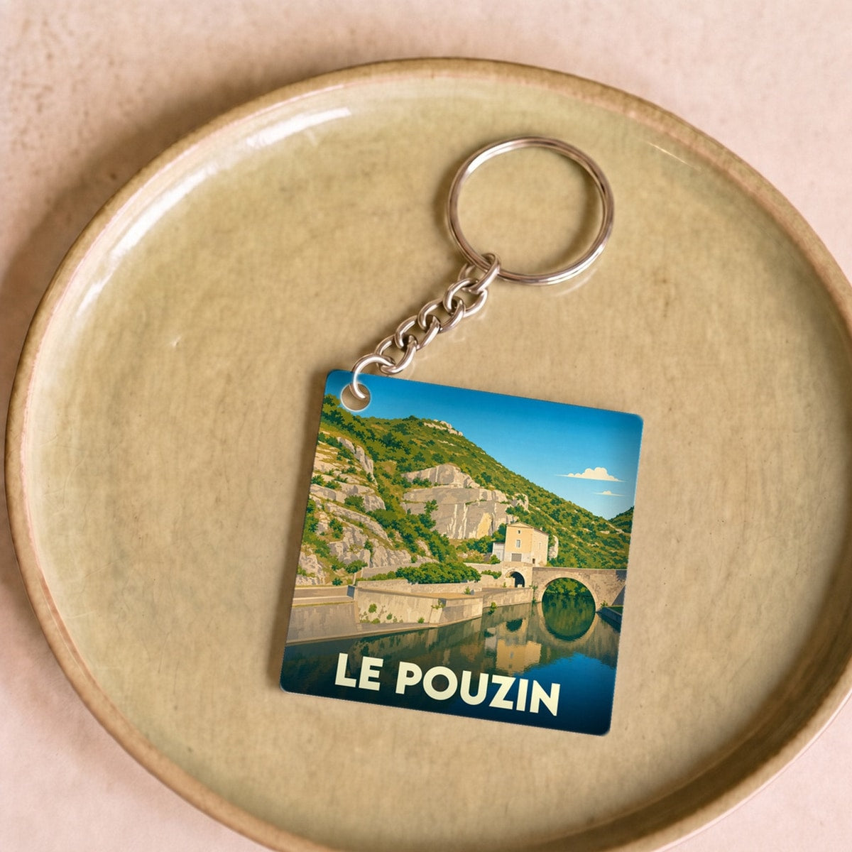 Porte-clés souvenir de la ville de Le Pouzin avec une illustration stylisée d'un pont se reflétant dans l'eau.