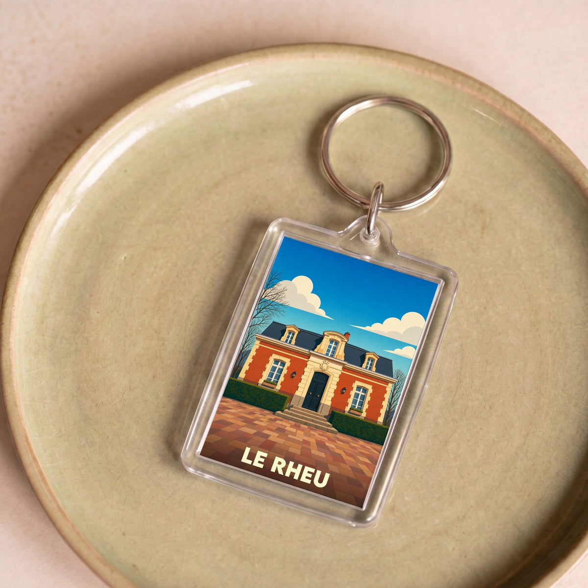 Porte-clés souvenir de la ville de Le Rheu avec une illustration stylisée d'un bâtiment historique.