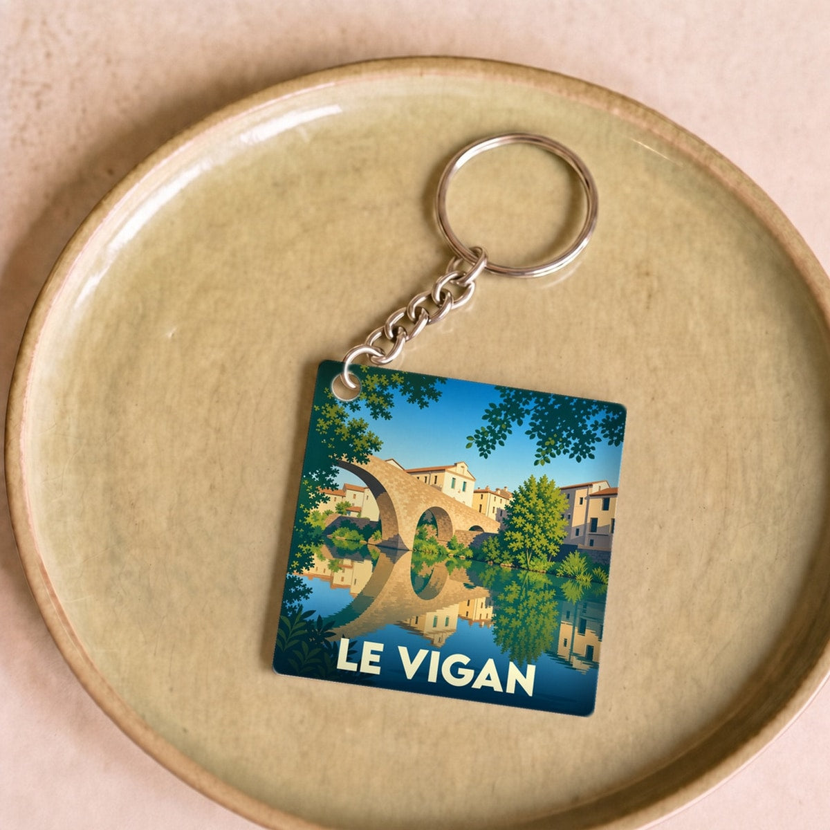 Porte-clés souvenir de la ville de Le Vigan avec une illustration stylisée de son vieux pont se reflétant dans l'eau.