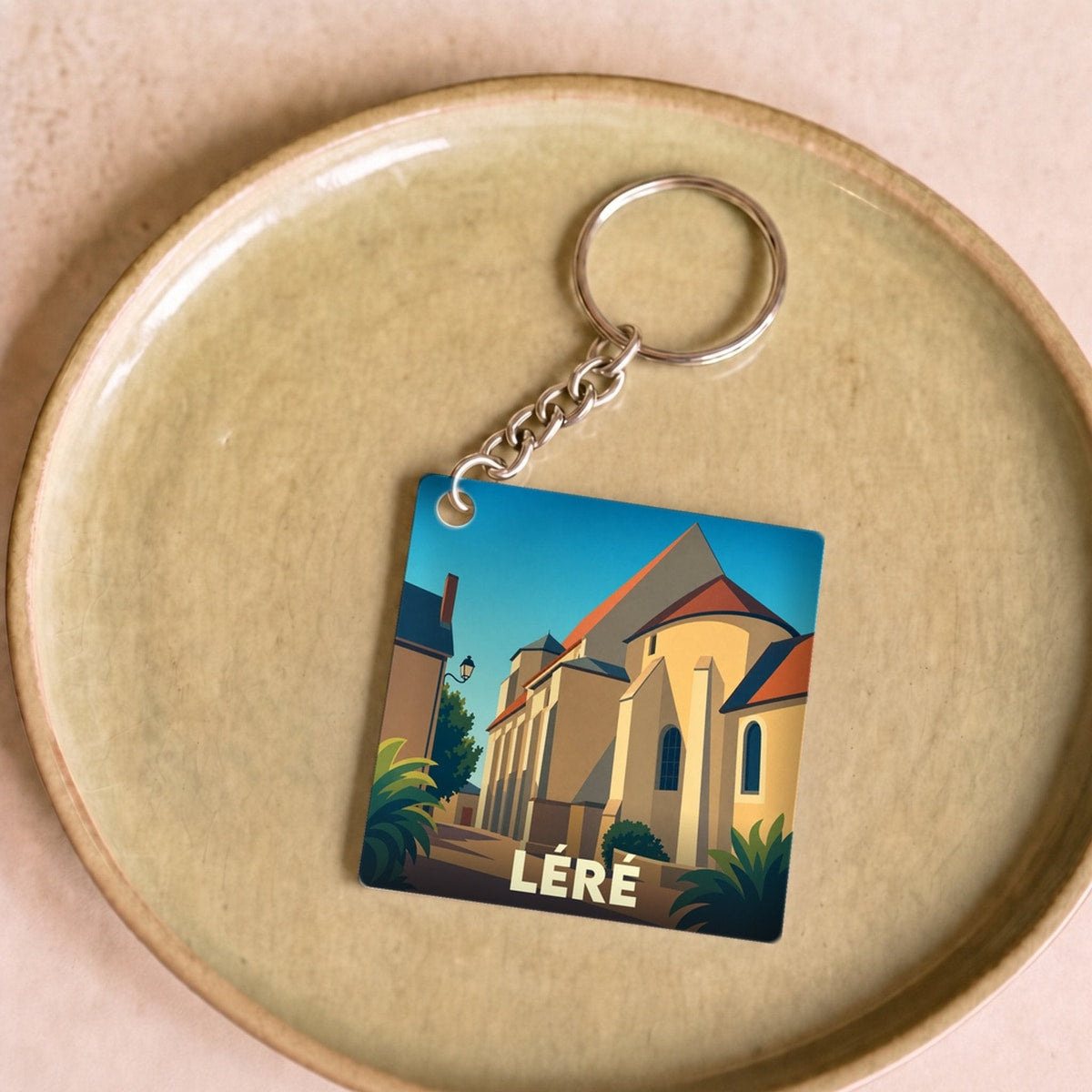 Porte-clés souvenir de la ville de Léré avec une illustration stylisée de son église sous un ciel bleu.