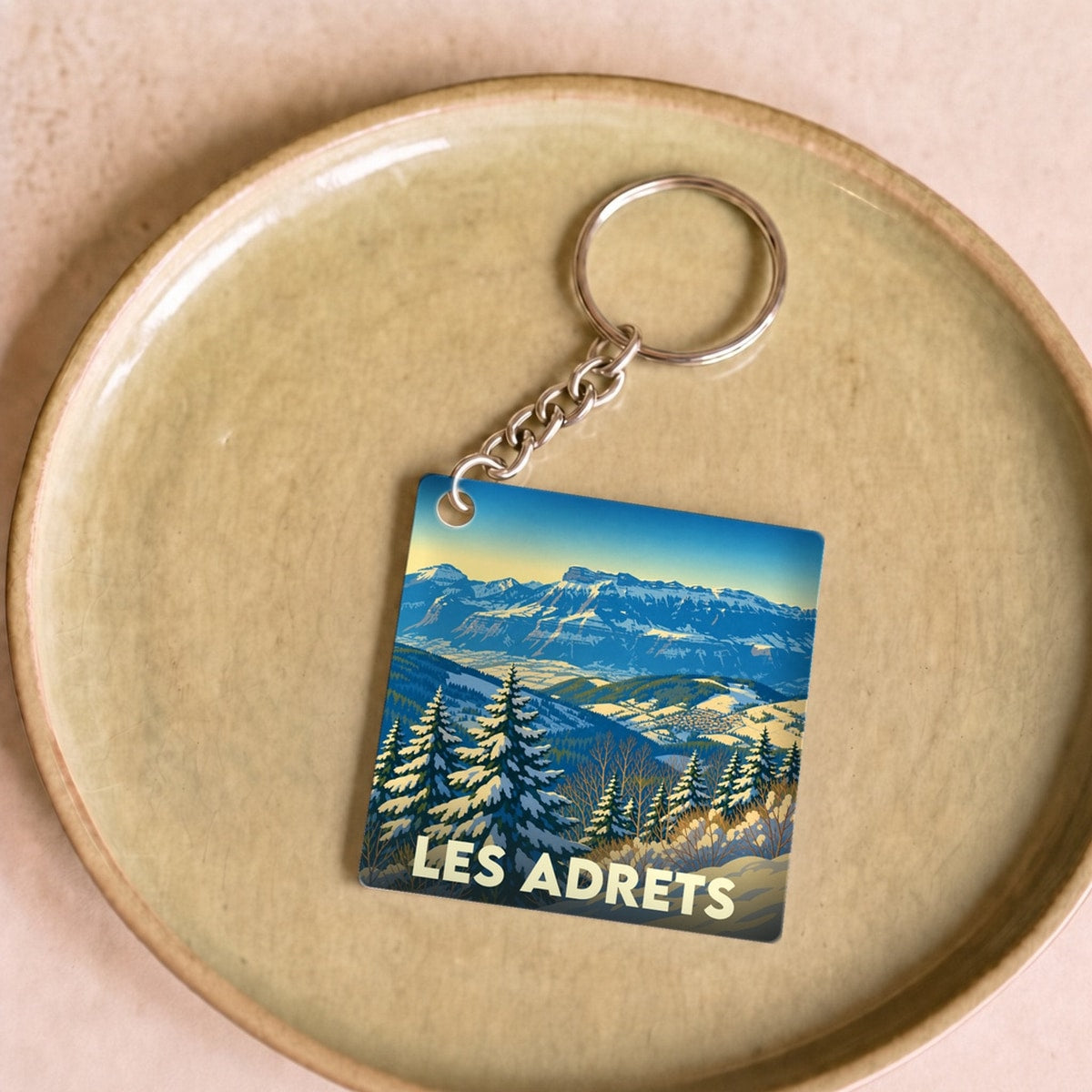 Porte-clés souvenir de la ville de Les Adrets avec une illustration de paysage montagneux enneigé.