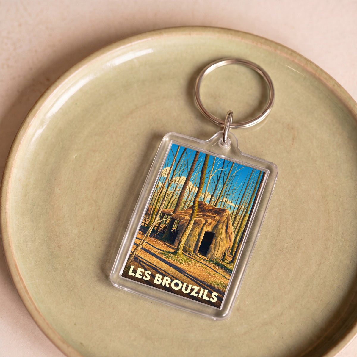 Porte-clés souvenir de la ville de Les Brouzils avec une illustration stylisée d'une cabane en forêt.