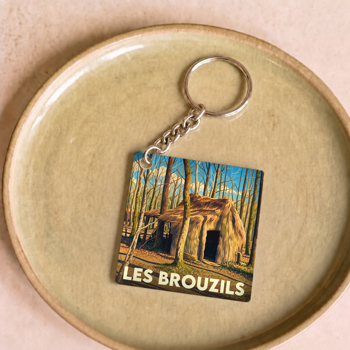 Porte-clés souvenir de la ville de Les Brouzils avec une illustration stylisée d'une cabane en forêt.