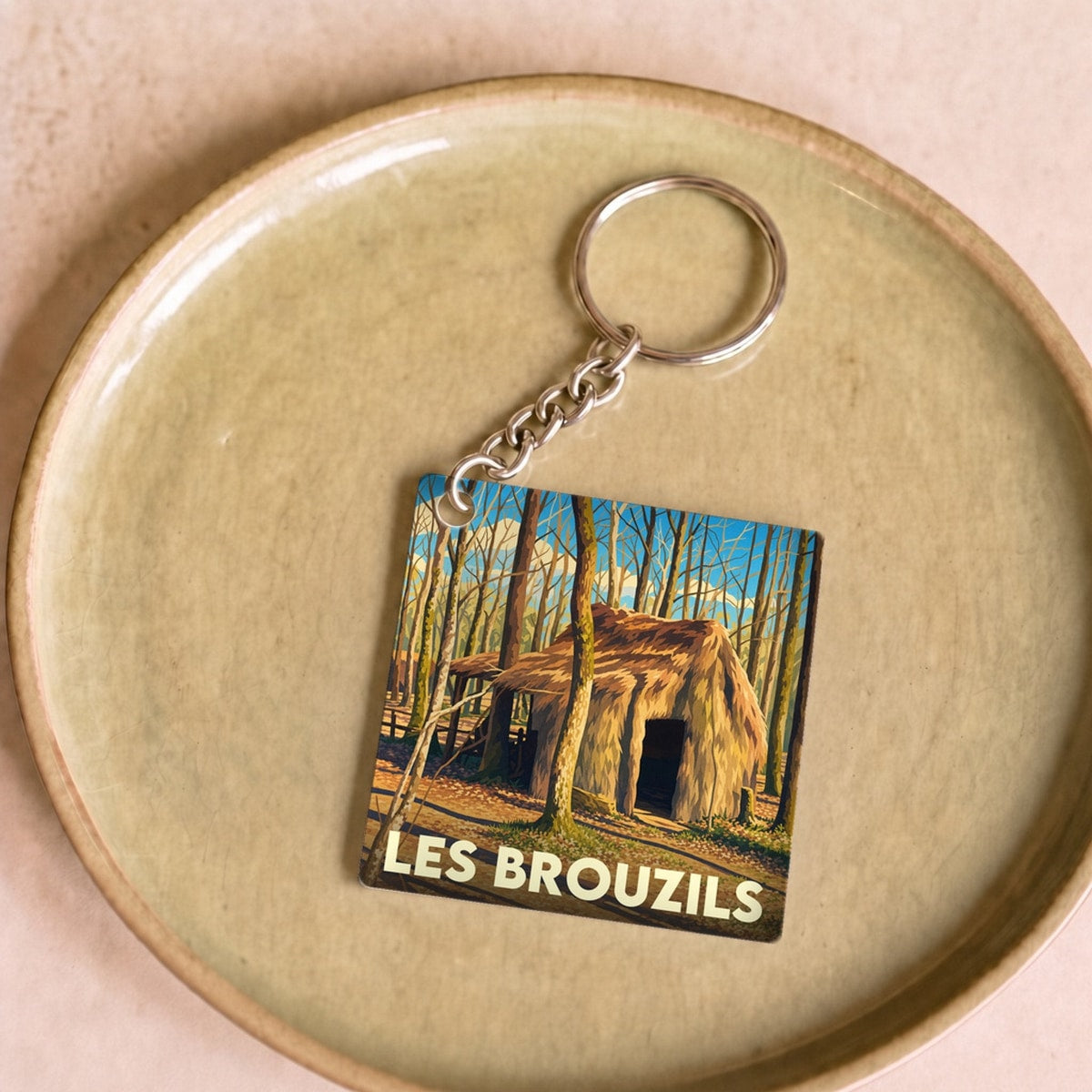 Porte-clés souvenir de la ville de Les Brouzils avec une illustration stylisée d'une cabane en forêt.