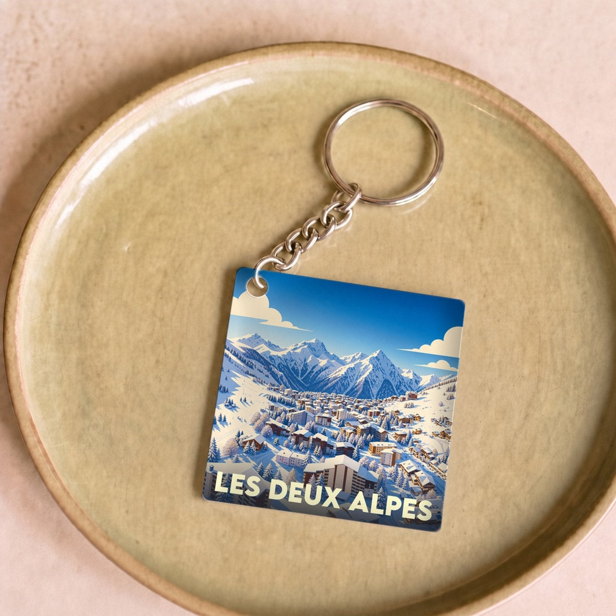 Porte-clés souvenir de la ville des Deux Alpes avec une illustration stylisée d'une station de ski enneigée.