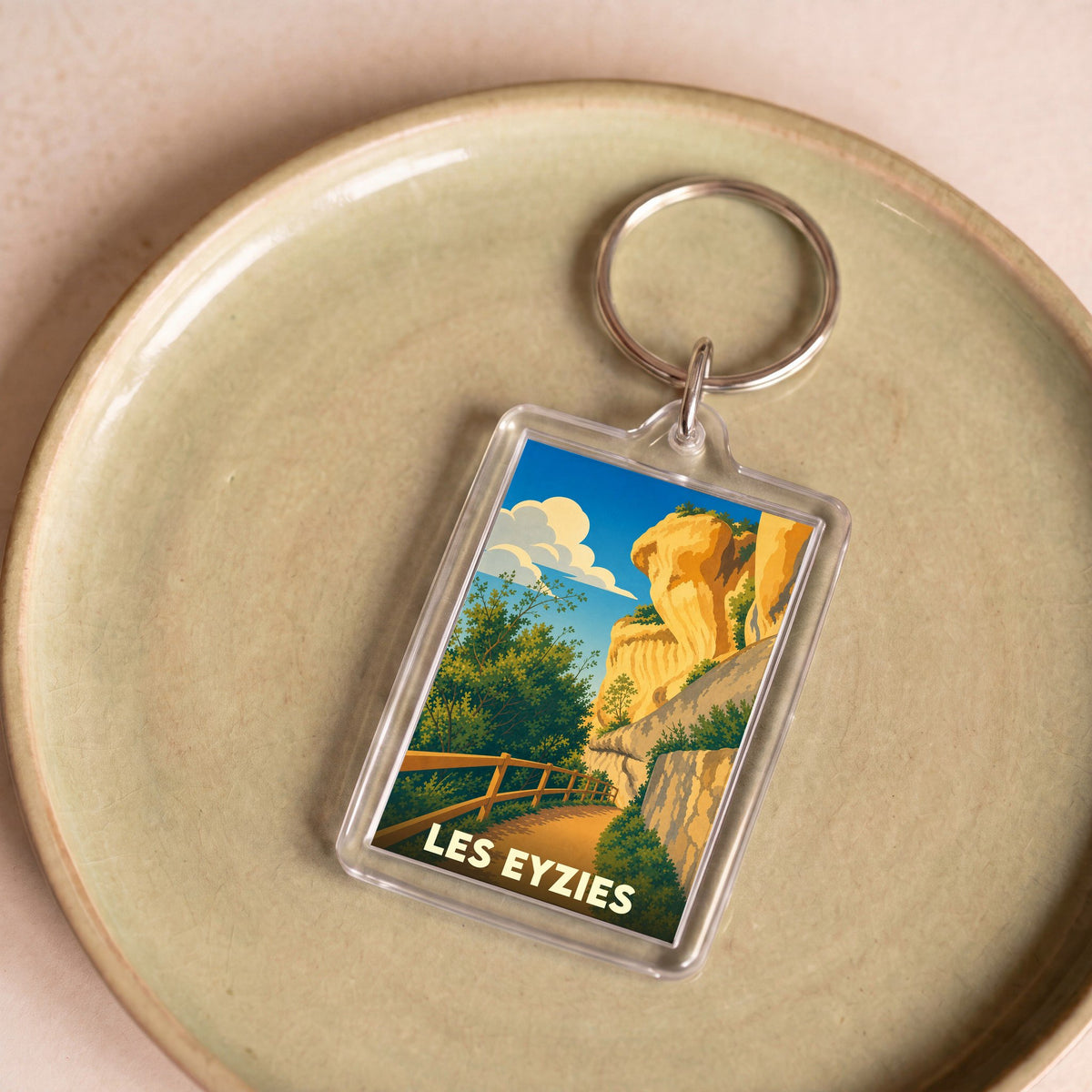 Porte-clés souvenir de la ville de Les Eyzies avec une illustration stylisée des falaises et de la végétation locale.