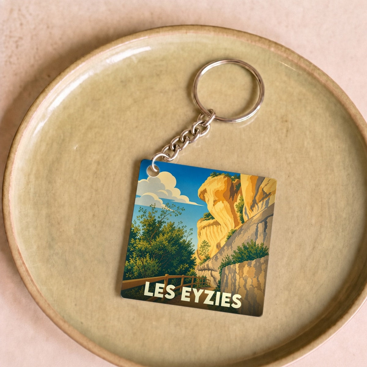 Porte-clés souvenir de la ville de Les Eyzies avec une illustration stylisée des falaises et de la végétation locale.