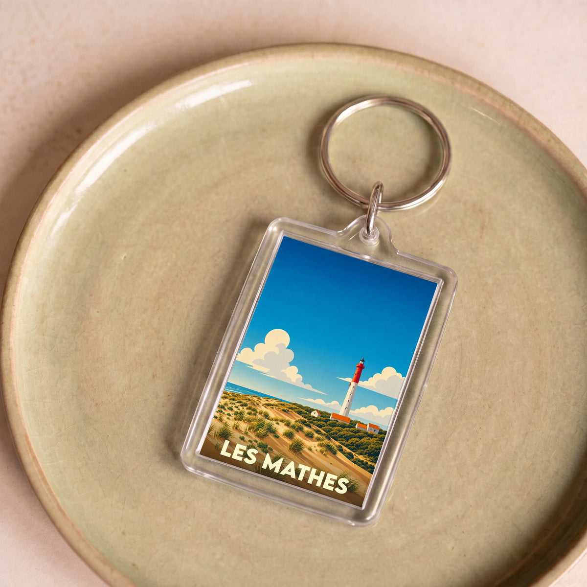 Porte-clés souvenir de la ville de Les Mathes avec une illustration stylisée d'un phare et de dunes.