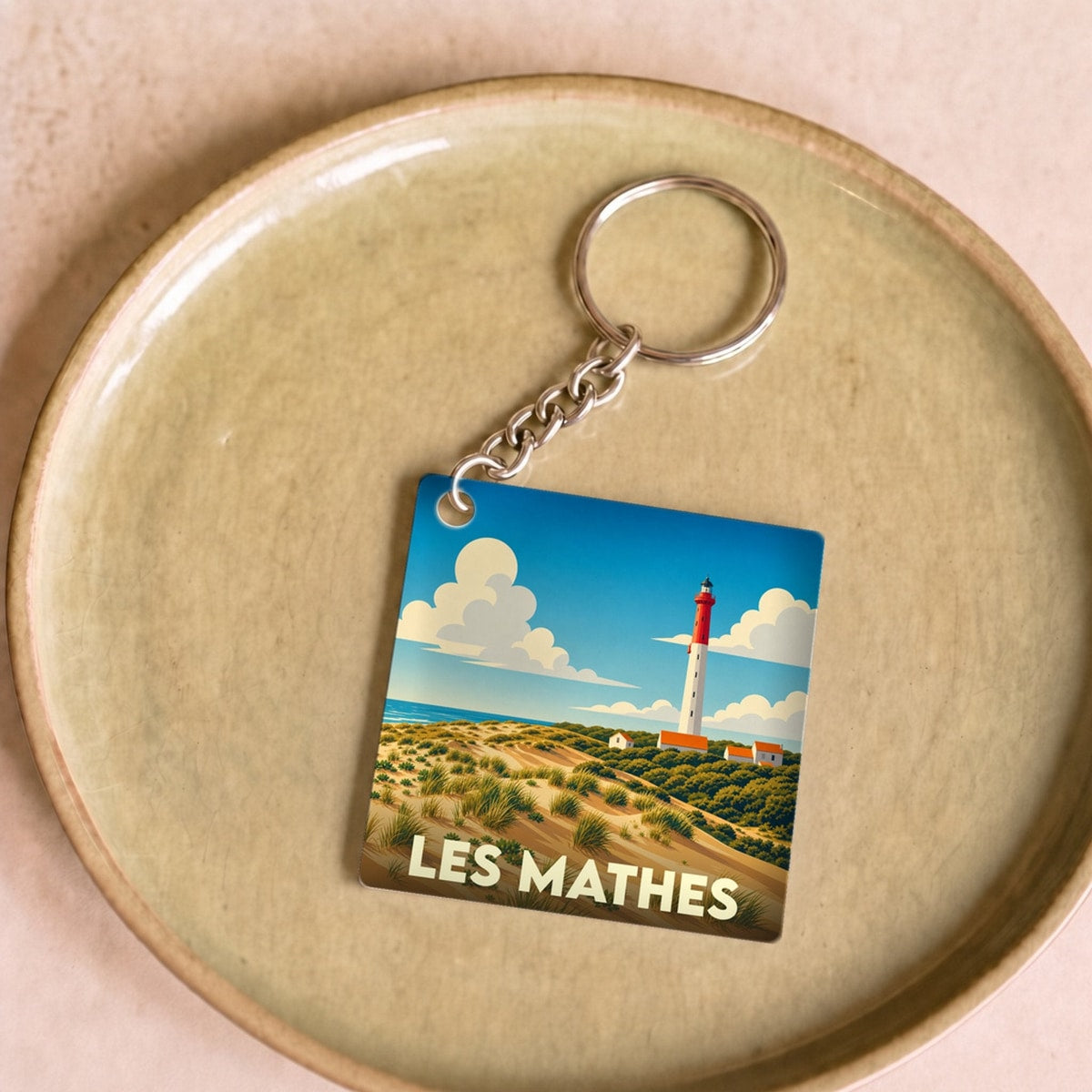 Porte-clés souvenir de la ville de Les Mathes avec une illustration stylisée d'un phare et de dunes.