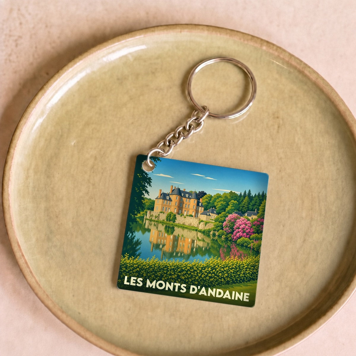 Porte-clés souvenir de la ville de Les Monts d'Andaine avec une illustration stylisée d'un château se reflétant dans l'eau.
