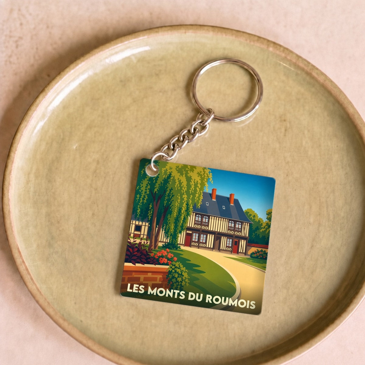 Porte-clés souvenir de la commune de Les Monts du Roumois avec une illustration stylisée d'une maison traditionnelle.
