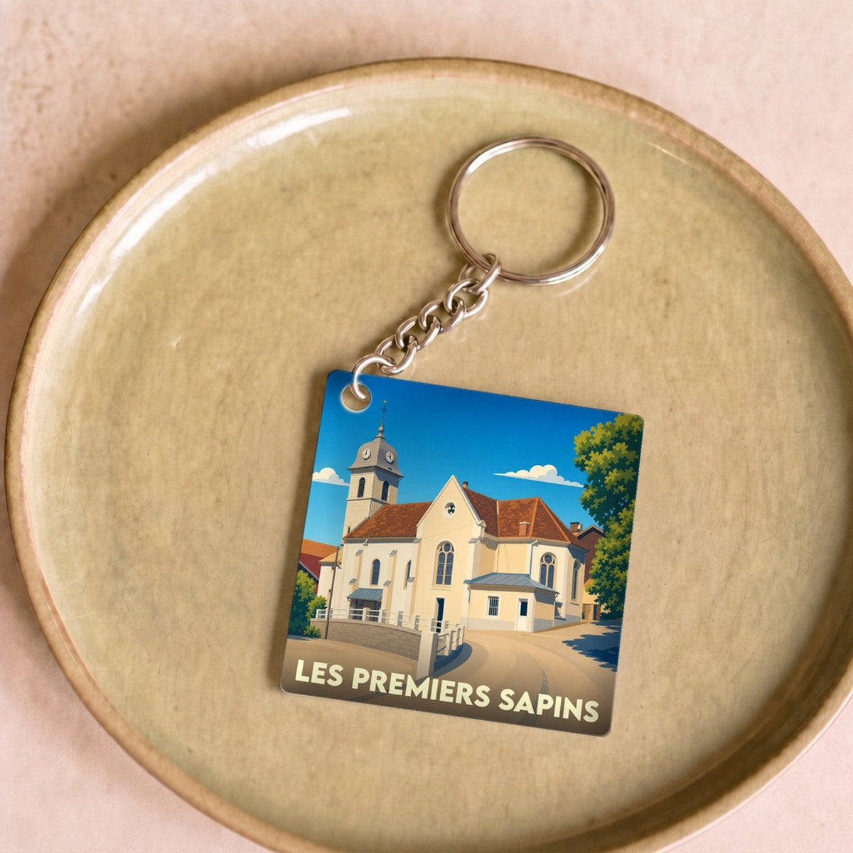 Porte-clés souvenir de la ville de Les Premiers Sapins avec une illustration stylisée de son église.