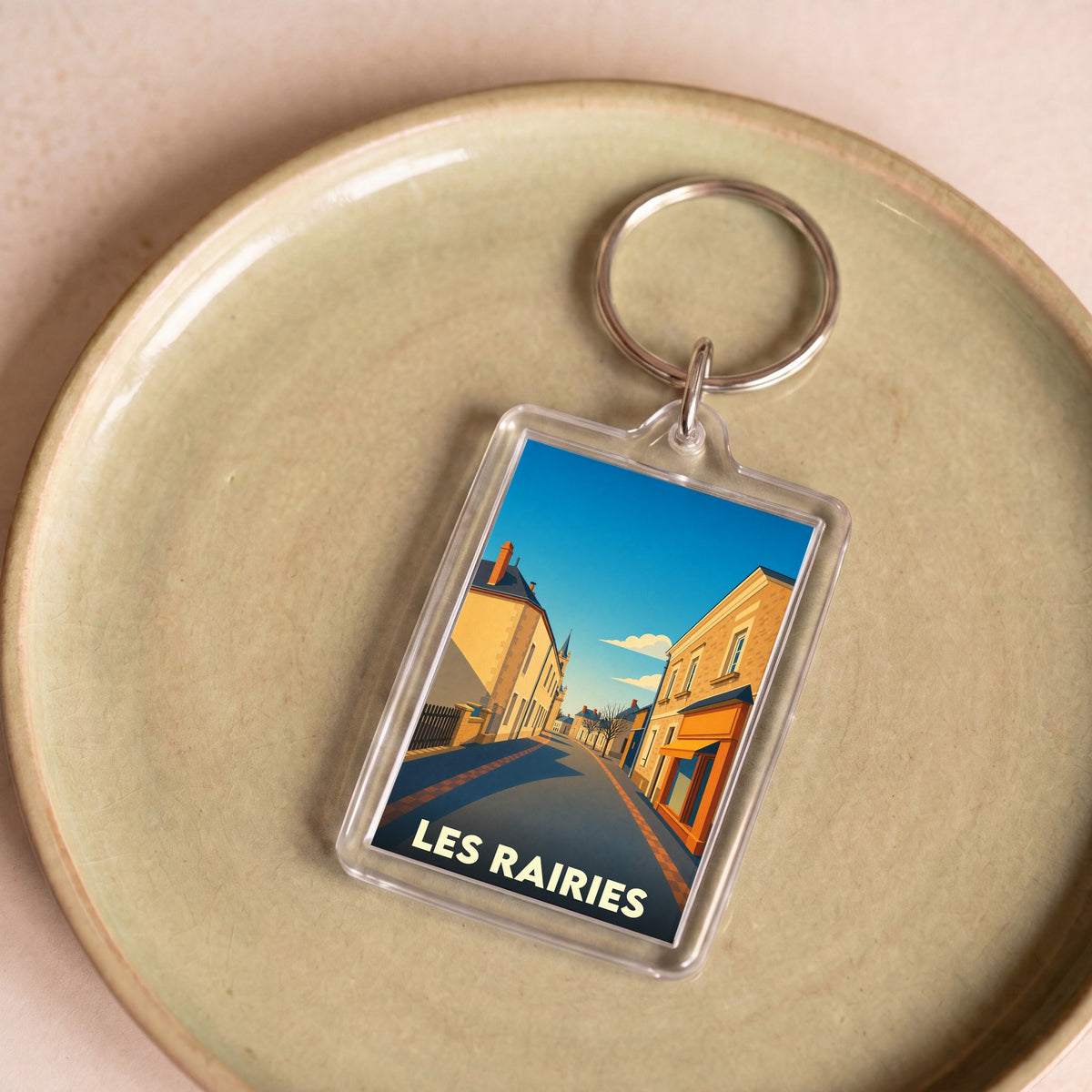 Porte-clés souvenir de la ville de Les Rairies avec une illustration stylisée d'une rue ensoleillée.