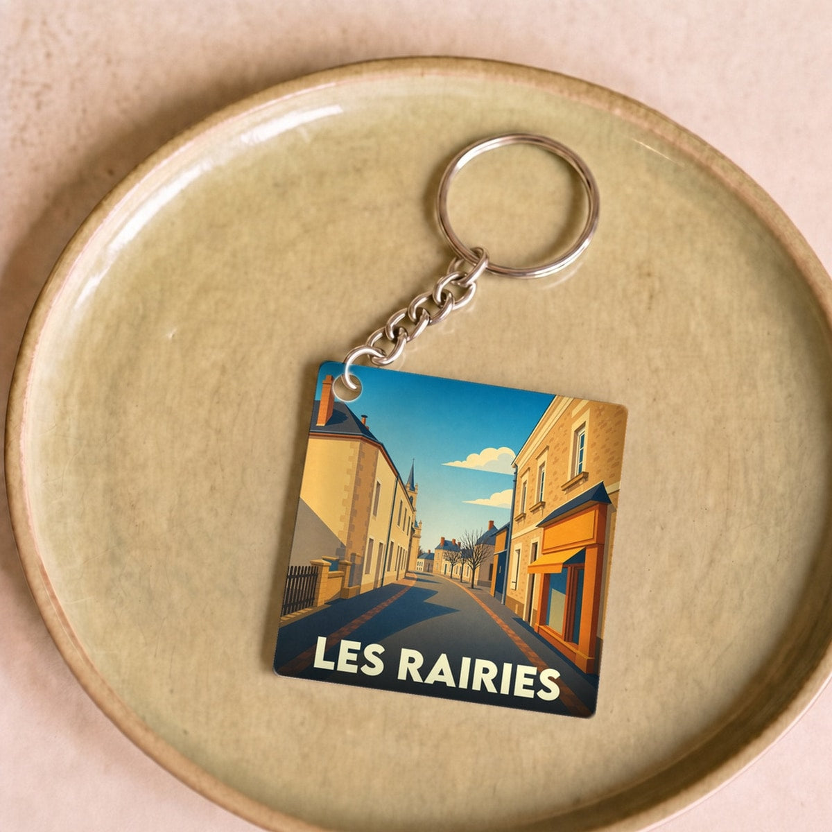 Porte-clés souvenir de la ville de Les Rairies avec une illustration stylisée d'une rue ensoleillée.