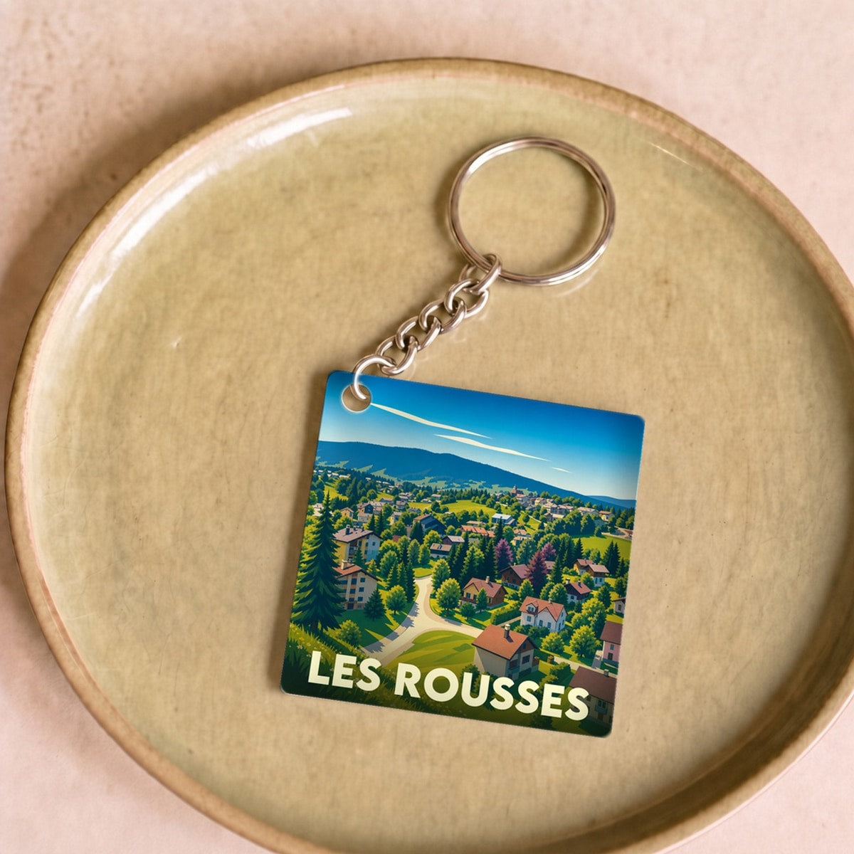 Porte-clés souvenir de la ville de Les Rousses avec une illustration stylisée de son paysage montagneux.