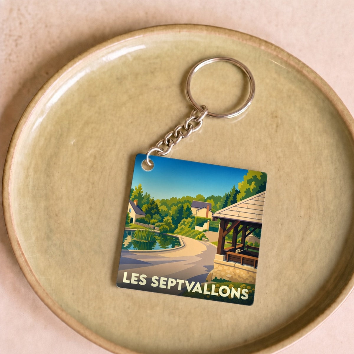 Porte-clés souvenir de la commune de Les Septvallons avec une illustration stylisée d'un paysage de village.