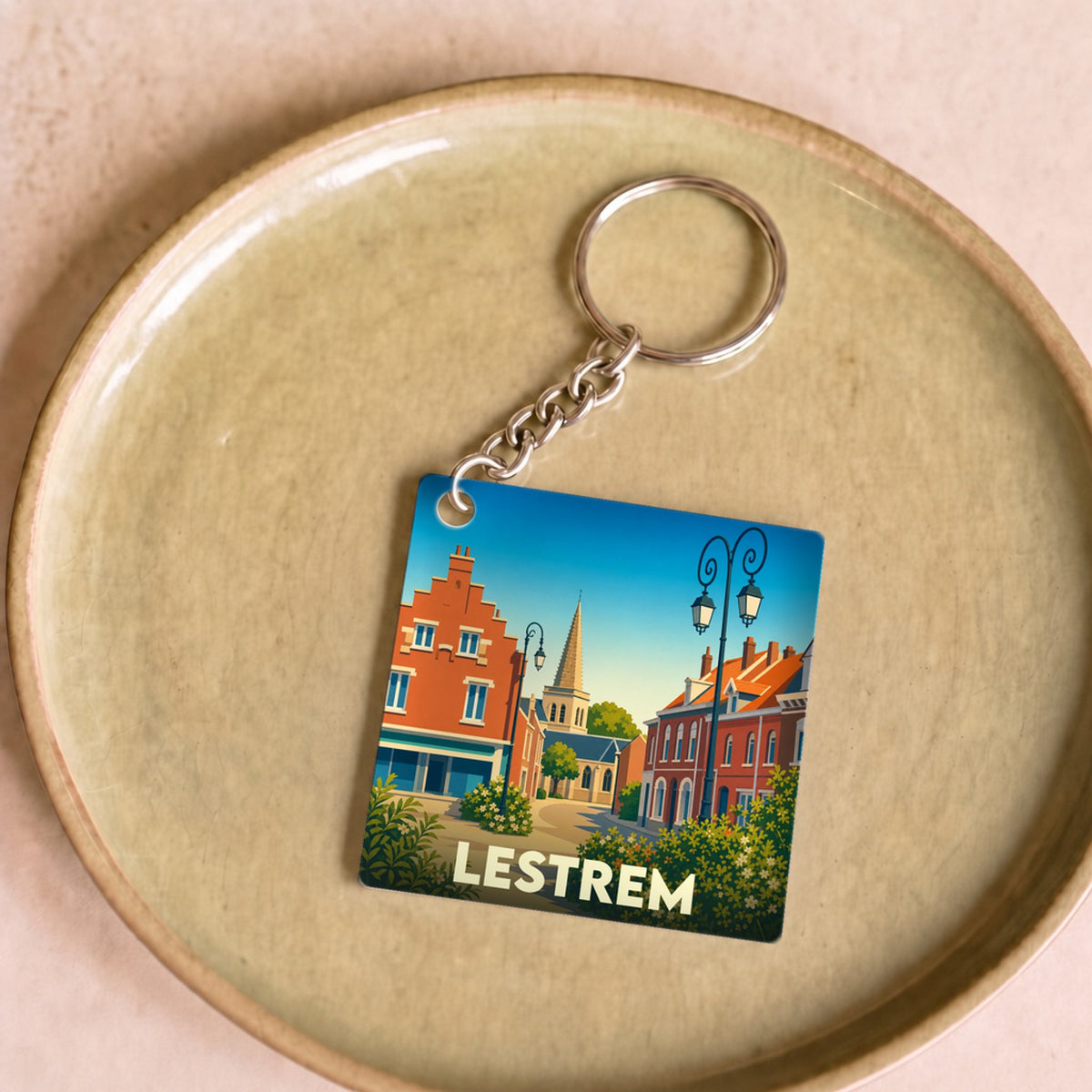 Porte-clés souvenir de la ville de Lestrem avec une illustration stylisée de ses rues et de son clocher.