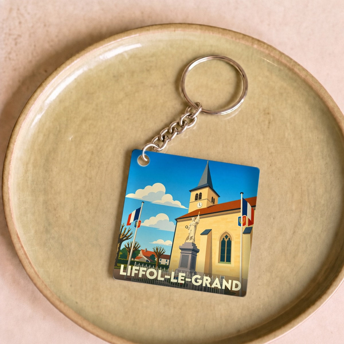 Porte-clés souvenir de la ville de Liffol-le-Grand avec une illustration stylisée de son église et de son monument.