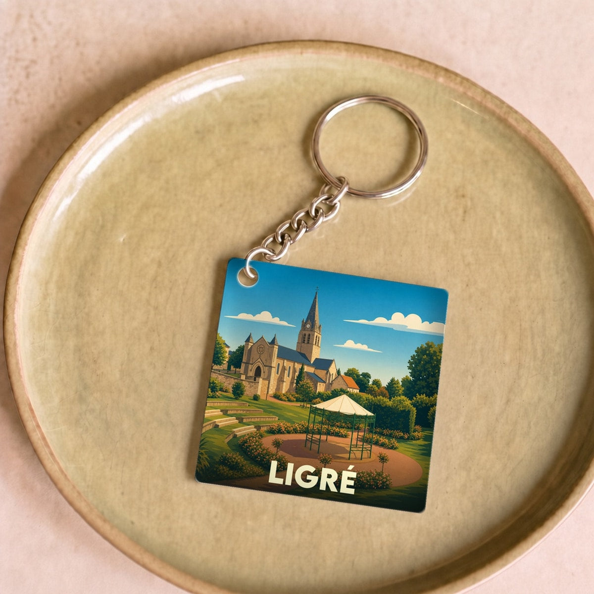Porte-clés souvenir de la ville de Ligré avec une illustration stylisée d'une église et son jardin.