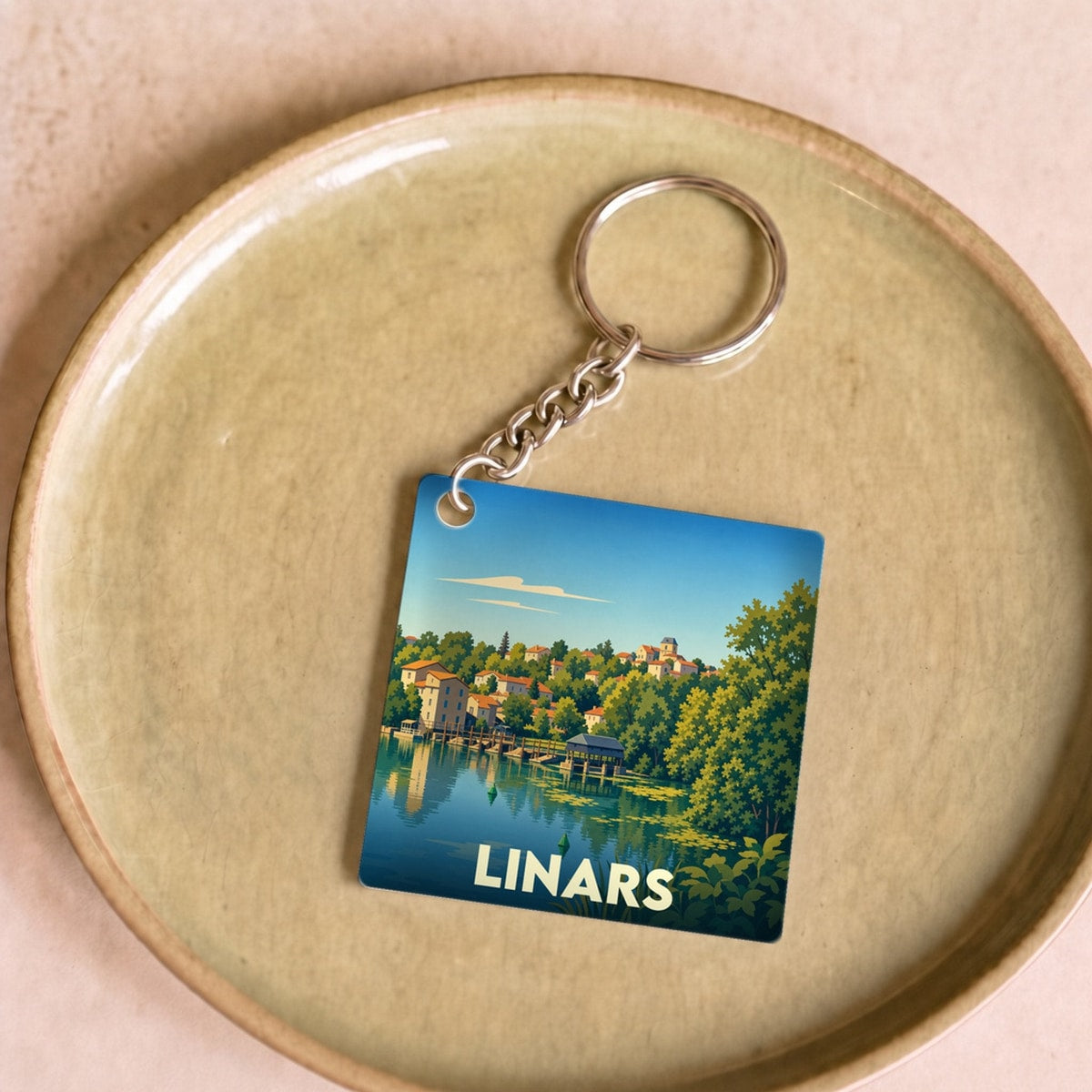 Porte-clés souvenir de la ville de Linars avec une illustration stylisée d'un paysage de bord de l'eau.