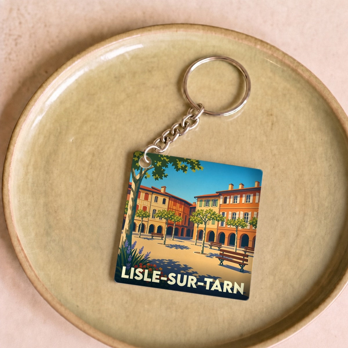Porte-clés souvenir de la ville de Lisle-sur-Tarn avec une illustration stylisée de sa place principale.