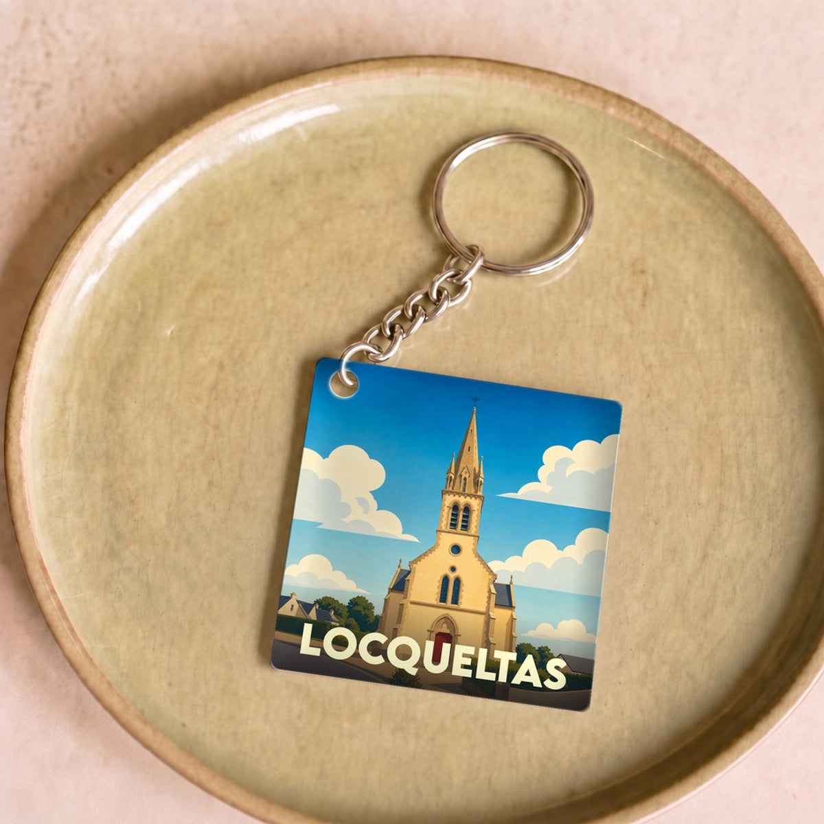 Porte-clés souvenir de la ville de Locqueltas avec une illustration stylisée de son église sous un ciel bleu.