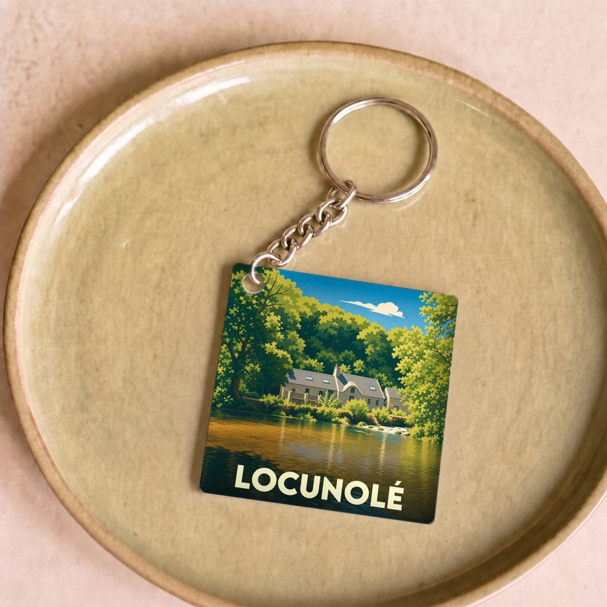 Porte-clés souvenir de la ville de Locunolé avec une illustration stylisée d'un paysage boisé au bord de l'eau.