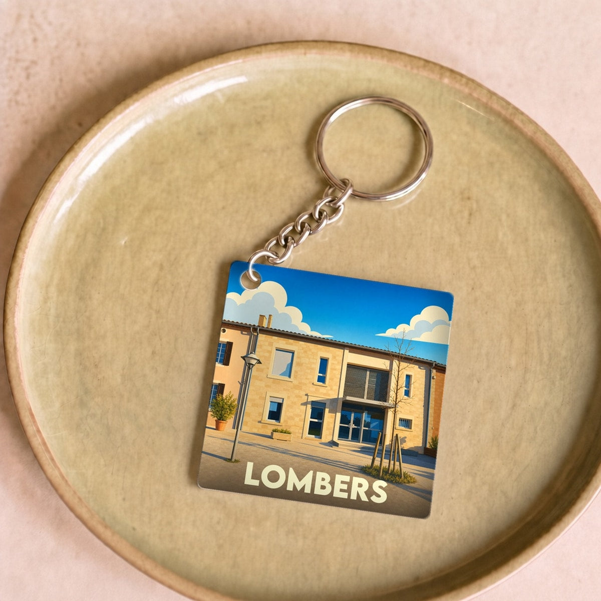 Porte-clés souvenir de la ville de Lombers avec une illustration stylisée d'un bâtiment local sous un ciel bleu.