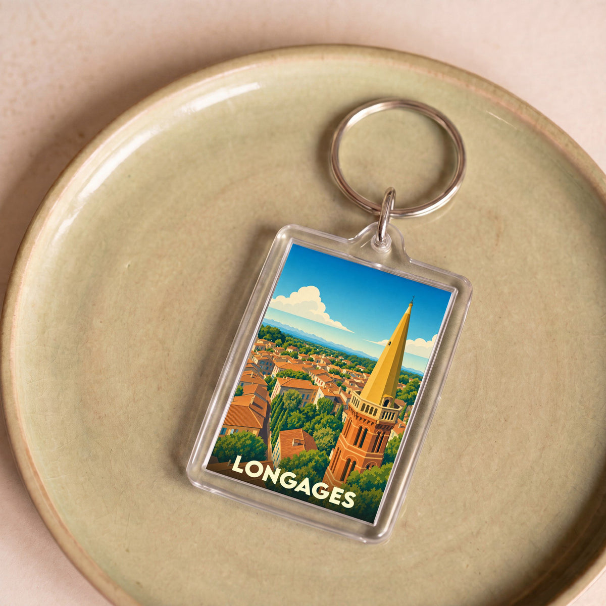 Porte-clés souvenir de la ville de Longages avec une illustration stylisée de son clocher et de ses toits.
