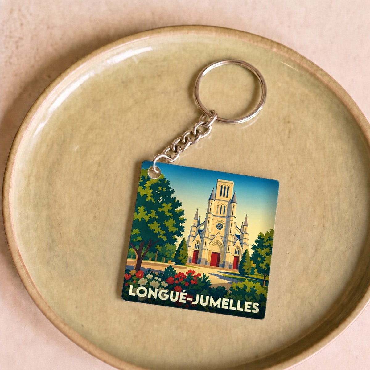 Porte-clés souvenir de la ville de Longué-Jumelles avec une illustration stylisée de son église et de jardins fleuris.