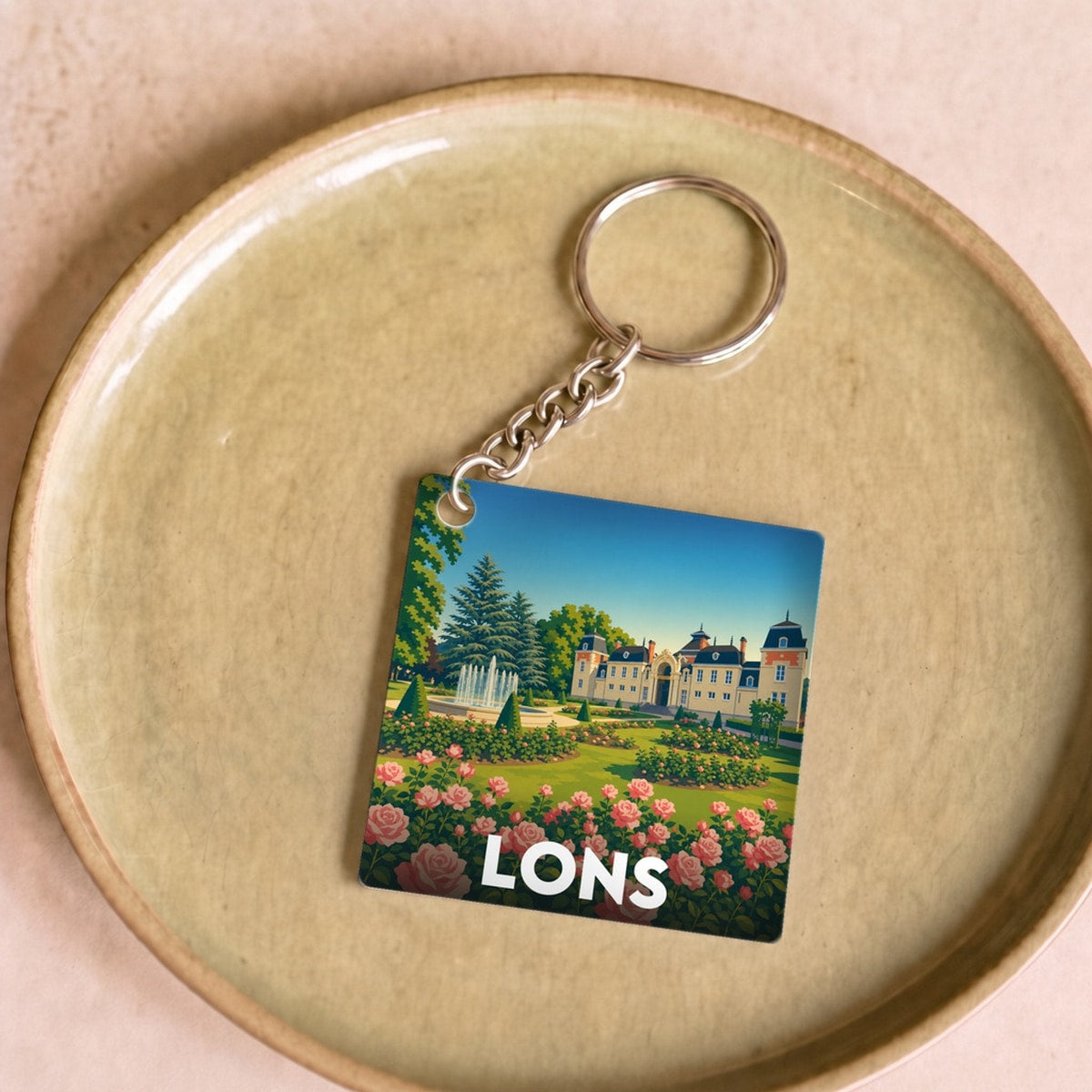 Porte-clés souvenir de la ville de Lons avec une illustration stylisée d'un parc fleuri et d'un château.