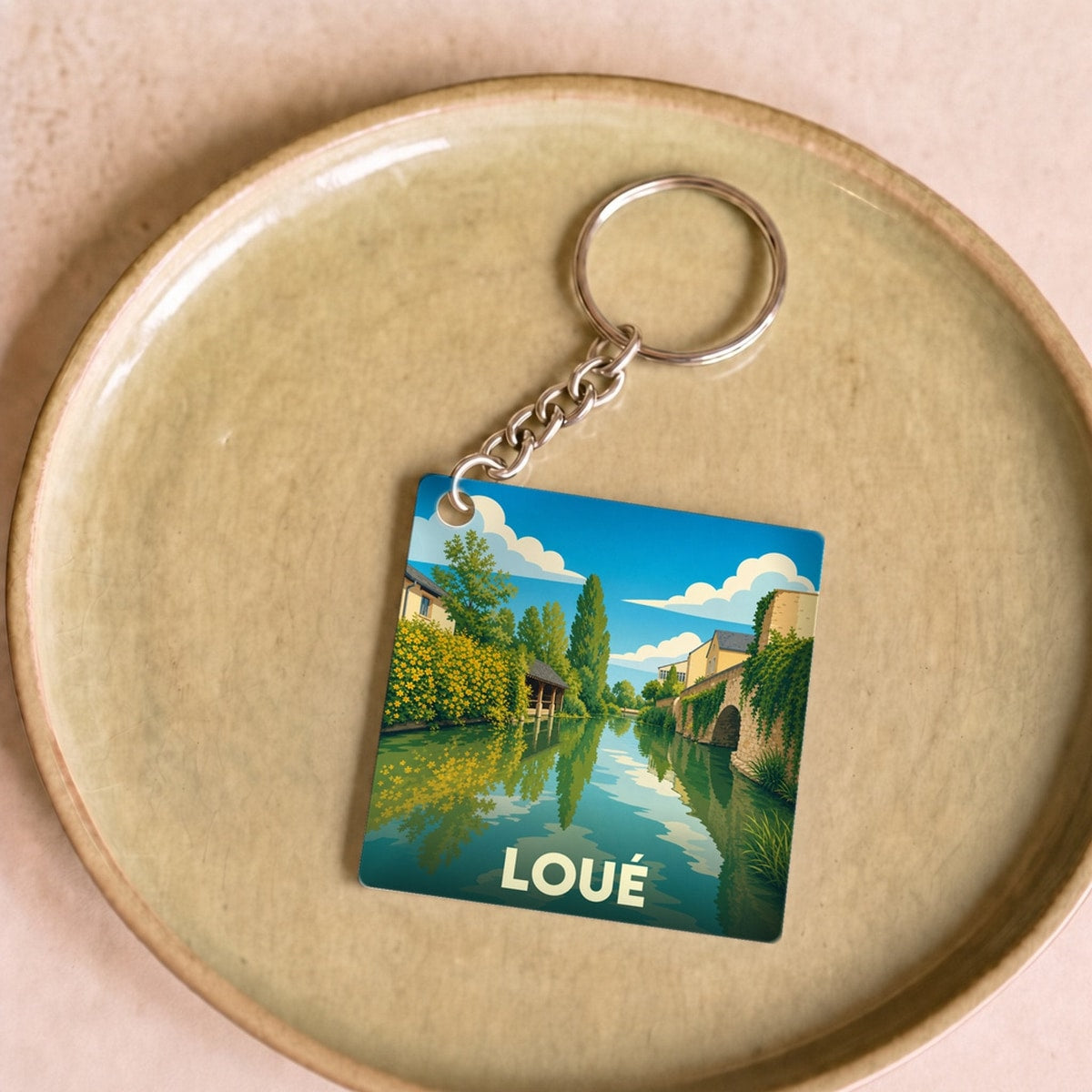 Porte-clés souvenir de la ville de Loué avec une illustration stylisée des bords de la rivière.