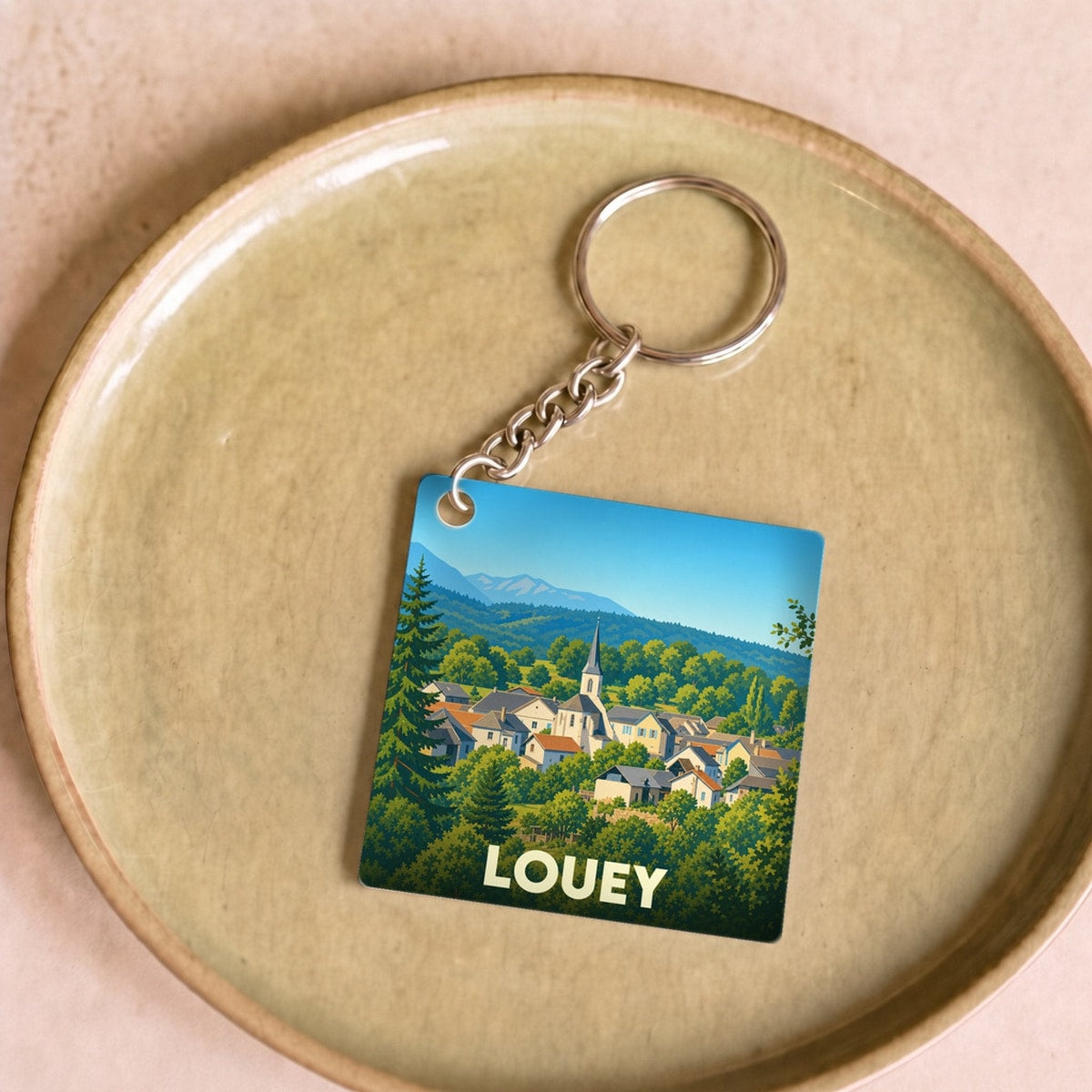 Porte-clés souvenir de la ville de Louey avec une illustration stylisée d'un village de montagne.
